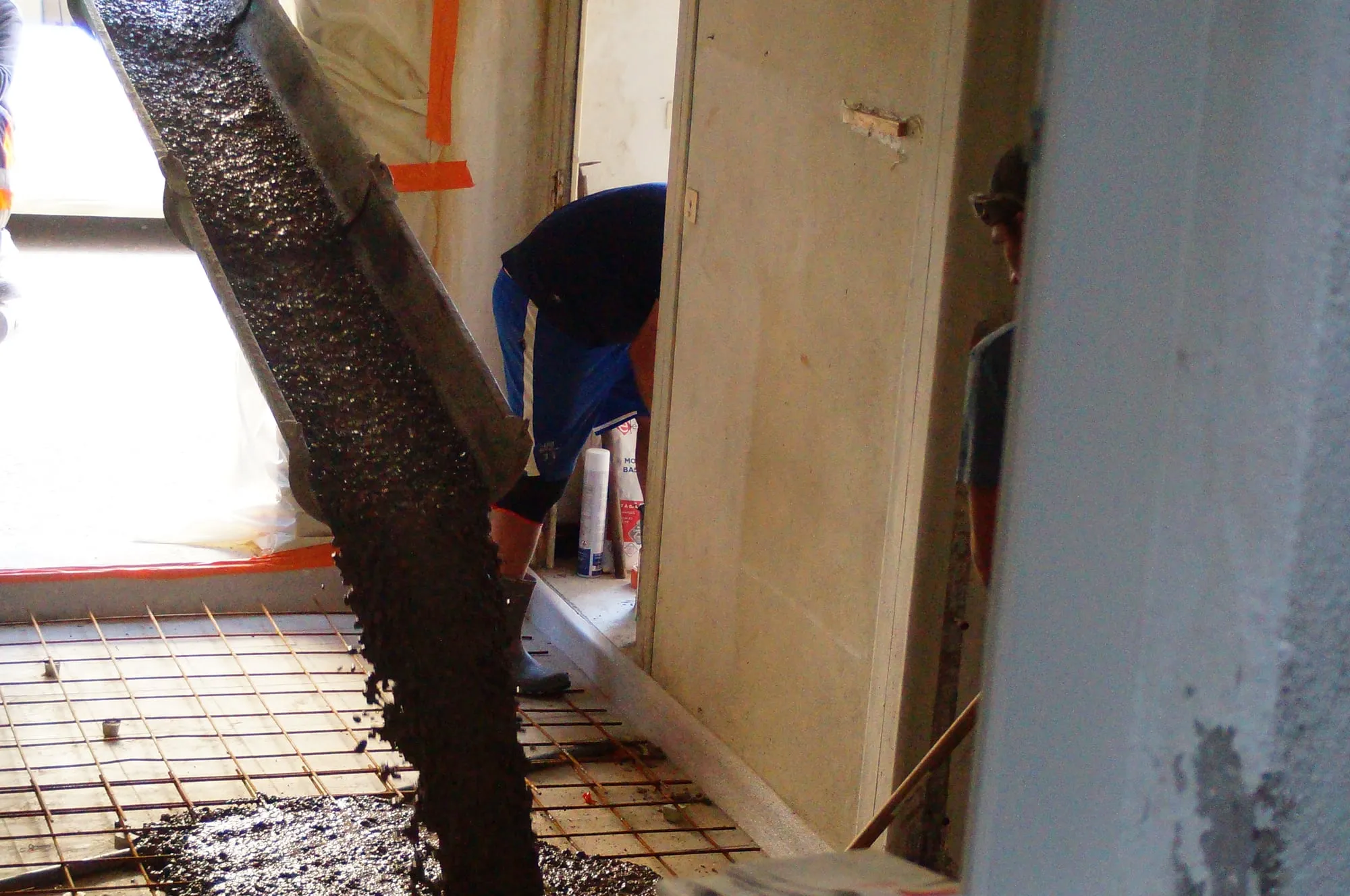 Béton coulé par la goulotte à travers une porte, sur le treillis