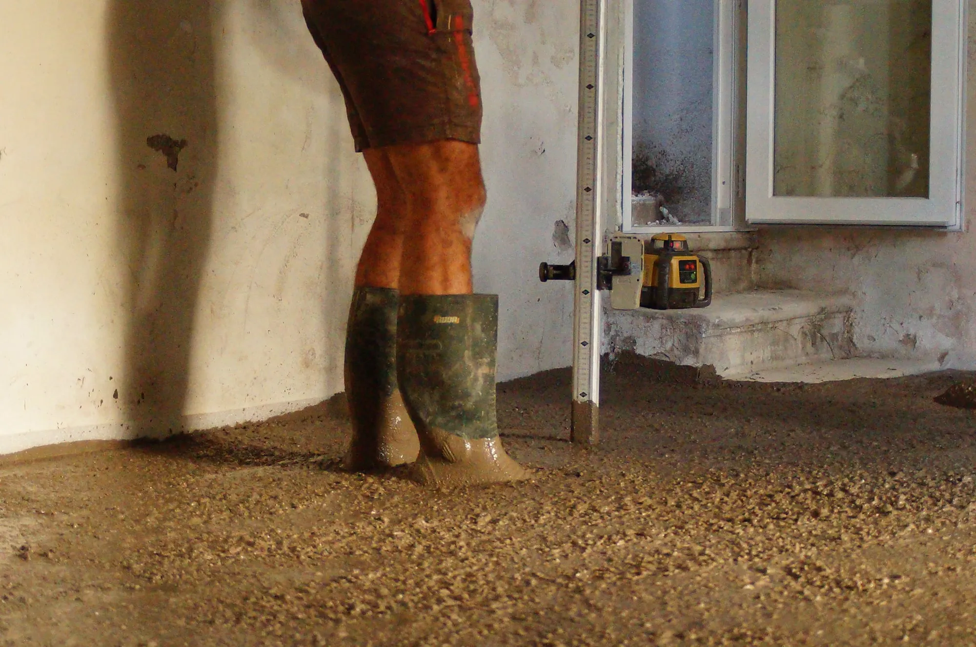 Bottes du maçon dans le béton frais, laser de niveau en arrière-plan