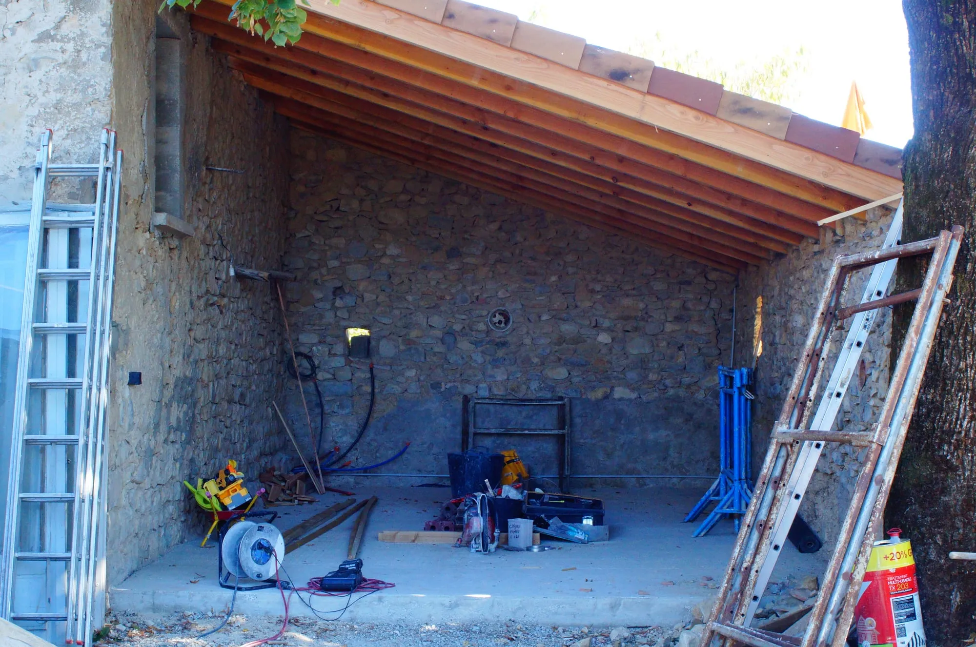 Cuisine d'été en chantier : murs en pierre, dalle coulée et charpente posée