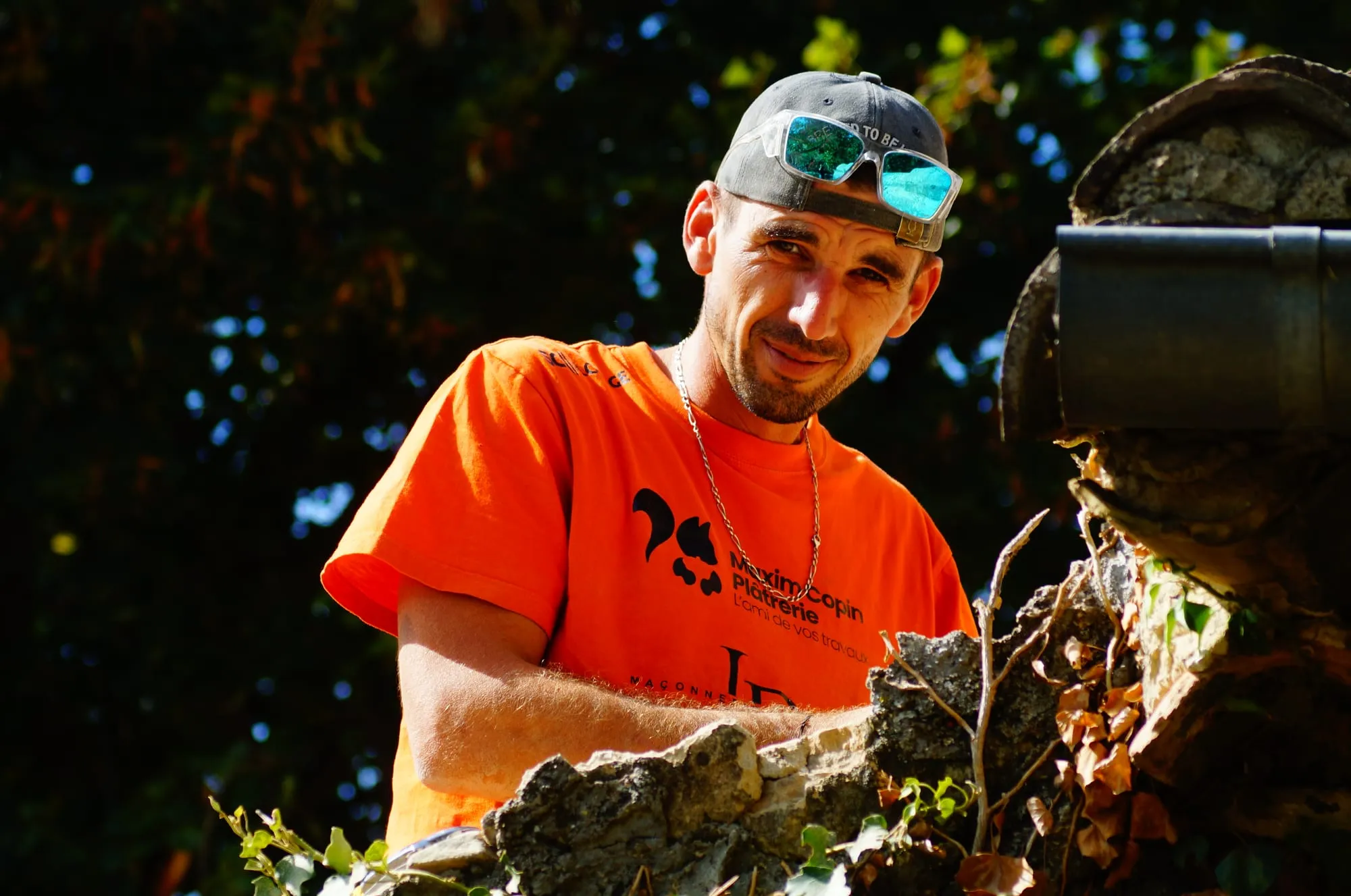 Maçon en t-shirt JR devant un mur en pierre, perceuse en main