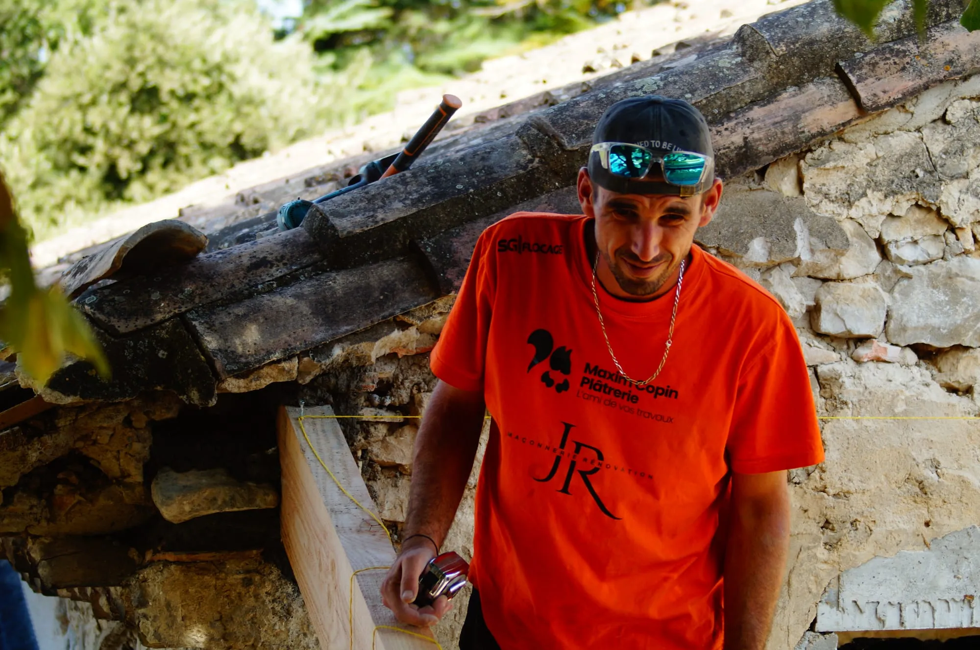 Maçon souriant devant le mur en pierre et sa poutre de rive
