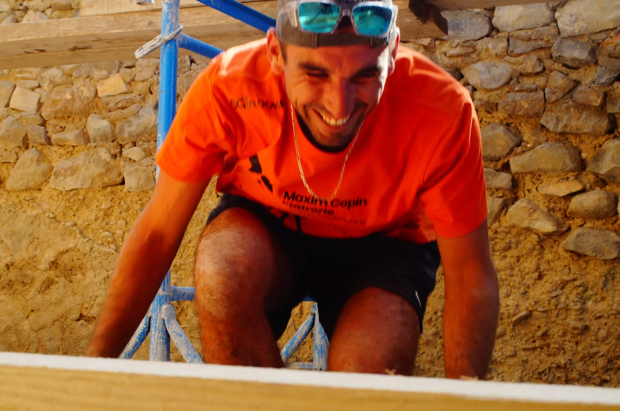Maçon souriant, accroupi devant le mur en pierre qu’il monte