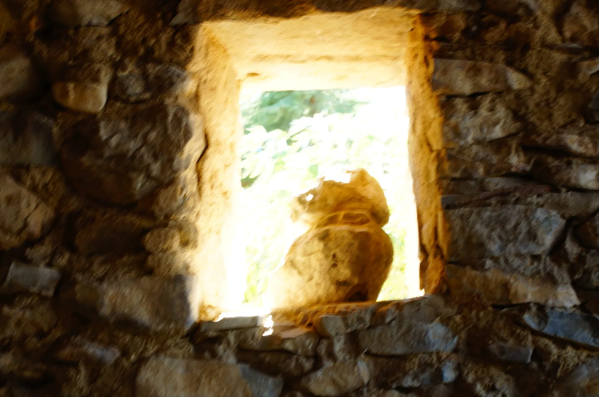 Petite ouverture dans un mur en pierre, baignée de lumière